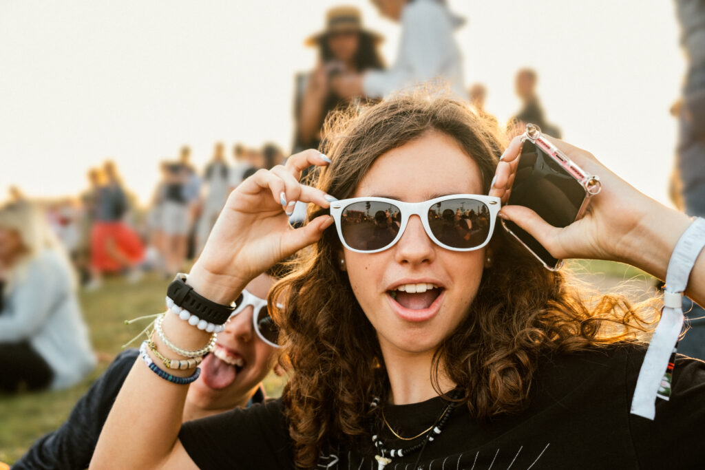 Pige med hvide solbriller på i sommervejret på en festival.