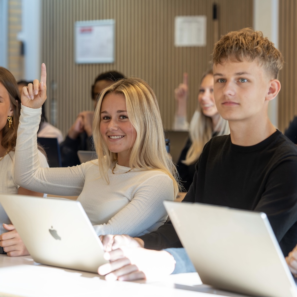Elever der har undervisning. Pige der rækker hånden op. Dreng sidder ved siden af.