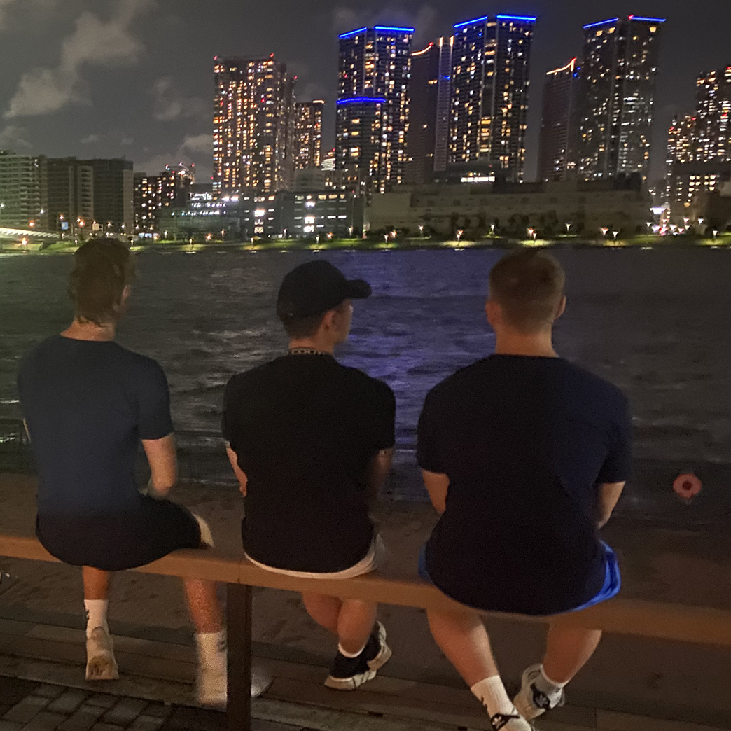 Tre drenge fra Slotshaven Gymnasium sidder med ryggen til kameraret og kigger ud over vandet. Der ligger højhuse i horisonten.