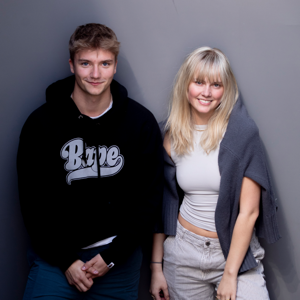 To tidligere elever fra Slotshaven Gymnasium, der står op af en grå væg og poserer for kameraret.