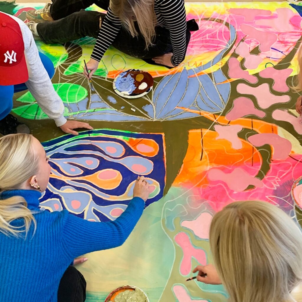 Fire elever fra Slotshaven Gymnasium er i gang med at male et stort billede. De sidder på gulvet og maler med mange farver.