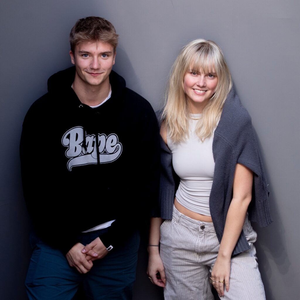 To tidligere elever på Slotshaven Gymnasium, står op af en grå væg og poserer for kameraet.