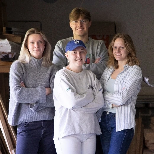 Fire elever fra Slotshaven Gymnasium står og poserer for kameraret med byggematerialer i baggrunden.