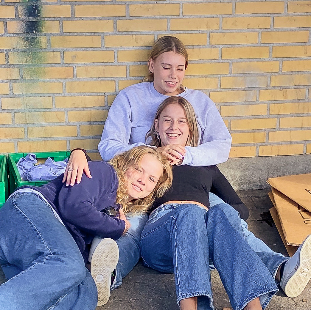 Tre piger fra Slotshaven Gymnasium sidder sammen. Den ene pige sidder mellem benene på den anden, og den tredje piger ligger op af de to andre piger.